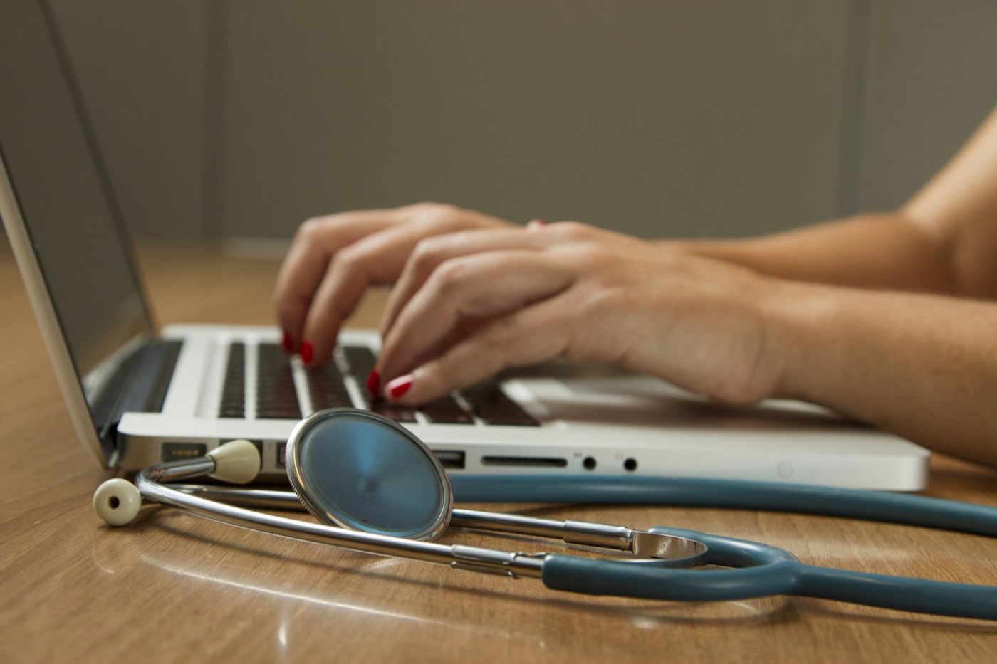 A laptop on a desk with a stethoscope resting beside it